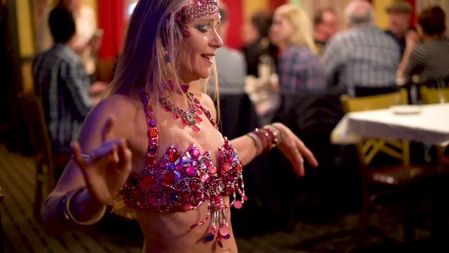 Slow motion extreme closeup of belly dancer doing shoulder chest shimmies in a restaurant.