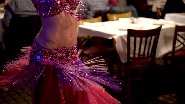 Slow motion closeup of rhinestone encrusted costume on belly dancer as she spins in a restaurant.