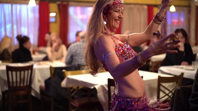 Slow motion closeup of smiling belly dancer doing hip thrusts in a restaurant.