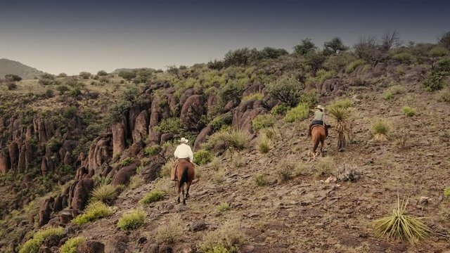 Aerial of two people on horseback exploring the edge of a rocky canyon in Texas, slow motion 24 fps.