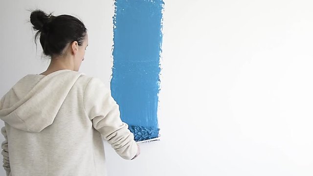 A model adult women painting a wall with blue paint