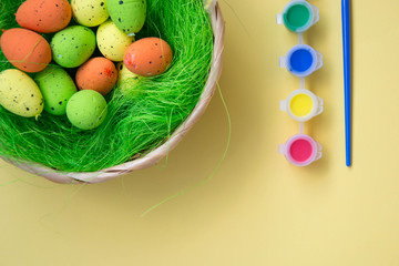 Green nest with colorful Easter eggs decoration on light yellow background. Easter concept, holiday tradition top view with colorful paints, copy space for text