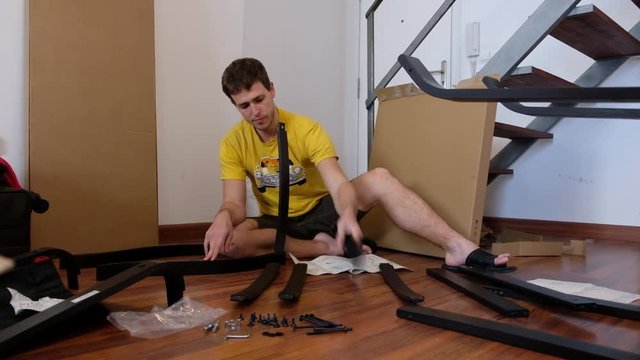 Assembling furniture. Young man is putting un-boxed pieces of a chair together.