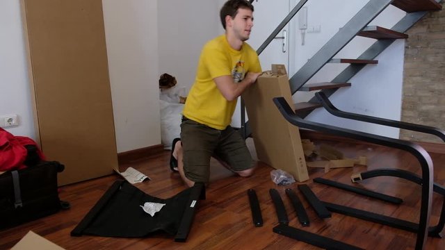 Young man is unpacking pieces of unassembled furniture from a cardboard box.
