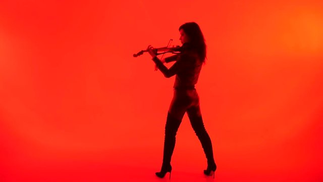 slim sensual young Asian girl in tight black leather clothes expressively plays the electric violin on a red background