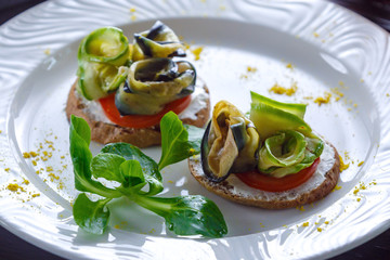 Sandwich of rolled eggplants and zucchini laid out on bread smeared with soft cheese and tomatoes.