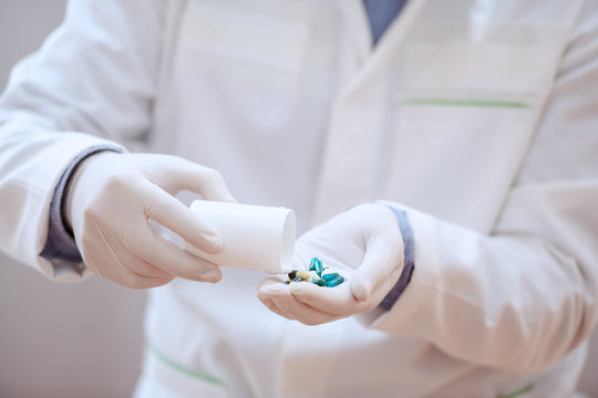 Close Up Of Caucasian Doctor In White Sterile Uniform And Hair Net On Head Holding Drugs In Hands.