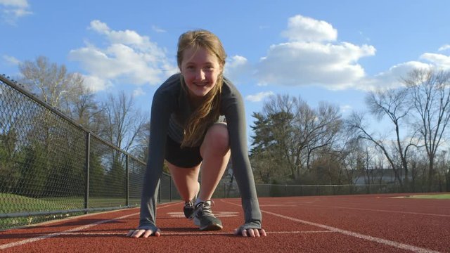 Teen girl in the ready position on a track smiles as she looks down the track