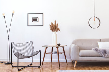 Stylish minimalistic living room with design grey sofa, black armchair, geometric lamp, retro table and elegant accessories Mock up posters frame on the white walls. Minimalistic home decor. 