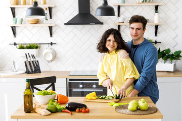 Young cute smiling couple cooking together at kitchen at home. A young woman slicing fresh vegetables on a wooden salad board. Cooking.