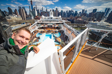 Young man makes selfie with huge cruise ship and New York city on background. Concept of happy vacation and travelling