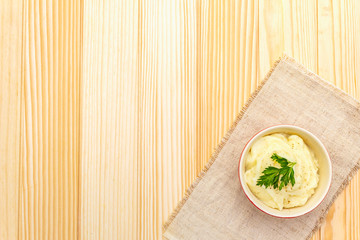 Warm mashed potatoes in a ceramic bowl with fresh parsley. On a vintage linen napkin on a stone background, top view, copy space.