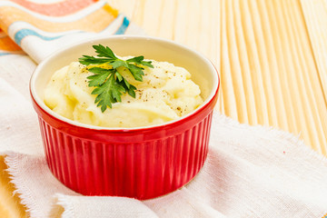 Warm mashed potatoes in a ceramic bowl with fresh parsley. On a vintage linen napkin on a stone background, close up.
