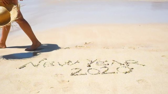 NEW YEAR 2020 EVE CONCEPT WITH TOURIST WOMAN WALKING ON THE SHORE AT THE BEAcH WITH THE WORDS WRITTEN ON THE SAND - People celebrating next year in tropical place for winter holiday