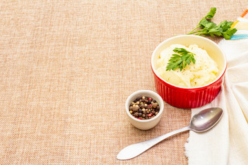 Warm mashed potatoes in a ceramic bowl with fresh parsley and dry pepper mix. On a linen cloth background, copy space.