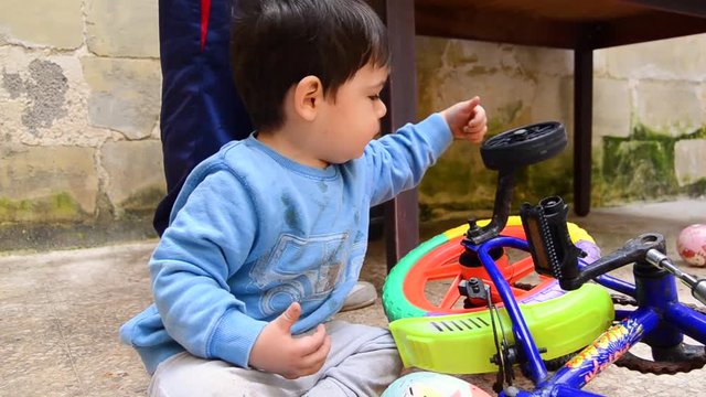 Cute playful male toddler playing with the wheel of his bicycle support