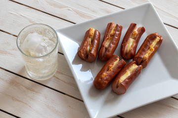 Roasted sausage with yellow cheese and a glass of soda over white wooden background
