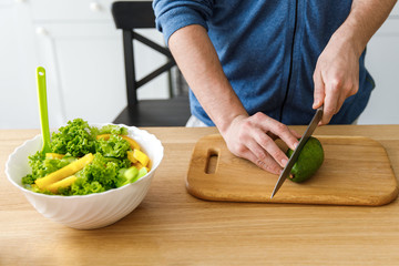 A young boy slicing an avocado on a wooden board for salad. Cooking