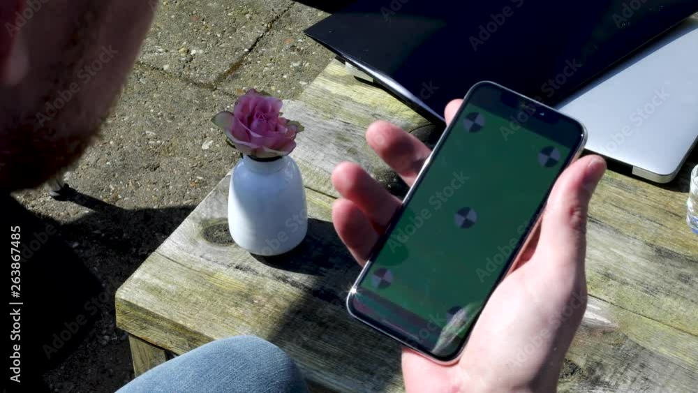 Poster close up on caucasian man hand holding smartphone or mobile phone in vertical position with green sc