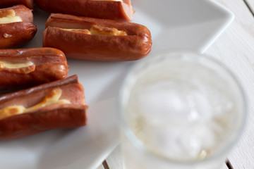 Roasted sausage with yellow cheese and a glass of soda over white wooden background