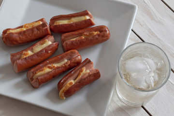 Roasted sausage with yellow cheese and a glass of soda over white wooden background