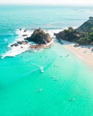 Aerial shot at sunrise over the ocean and white sand beach with swimmers and surfers enjoying summer