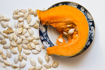 Close-up of a piece of orange pumpkin and seeds, indoors, white background