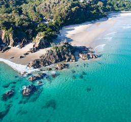 Aerial shot at sunrise over the ocean and white sand beach with swimmers and surfers enjoying summer