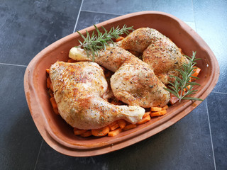 Three chicken legs on vegetables in a clay pot ready for being baked in the oven