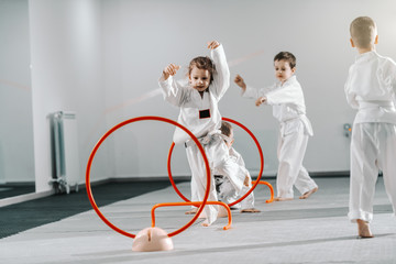Small group of Caucasian kids in doboks practicing taekwondo and warming up for treining while...