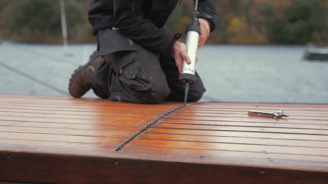 Young man seals planked roof of wooden boat with sika flex  waterproof mastic to seal out rain