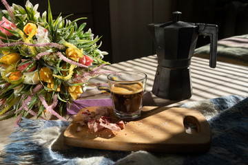 in bed, black coffee in a glass cup, a milk jug, crumbled pink chocolate on a blackboard and a bouquet of wildflowers, low light, horizontal frame