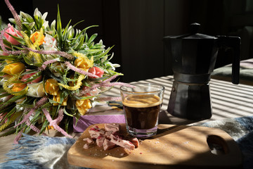 in bed, black coffee in a glass cup, a milk jug, crumbled pink chocolate on a blackboard and a...