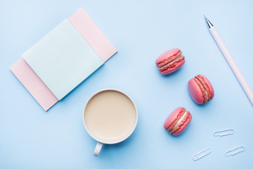 Concept morning Breakfast. Cup of coffee, macaroon cookies and notepad on blue pastel background. Flat lay style.