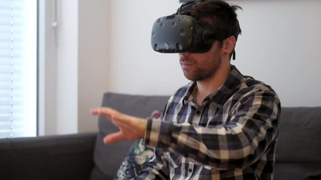 A medium shot of a white young male playing virtual reality while sitting on a couch without controllers