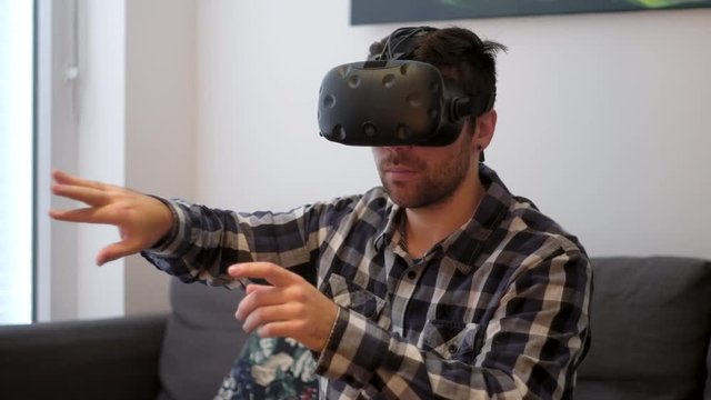 A medium shot of a young white male using Virtual Reality at home on a couch