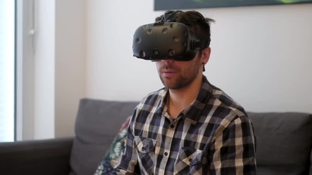 A medium shot of a young white male looking around with virtual reality while sitting on a couch