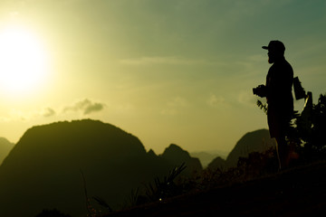 A young photographer with a beard and a cap meets the dawn on a high mountain.