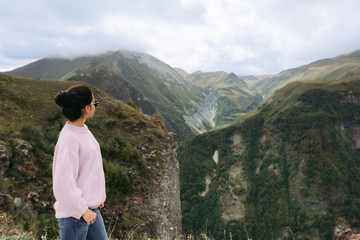 Naklejka premium young girl in a sweater is looking at the Caucasian mountains, Georgia, rear view. copy space