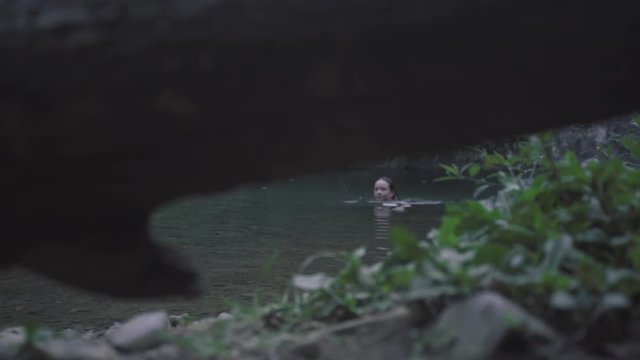 SLOW MOTION: watching from underneath a log as a girl swims then lifting over the log to watch the girl make her way out of Mango Waterfall in Adjuntas, Puerto Rico.