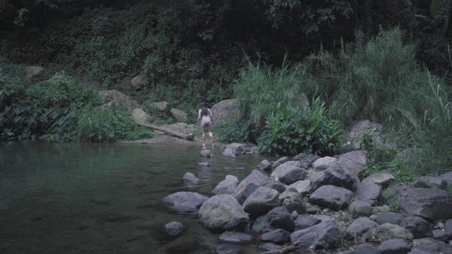 SLOW MOTION: lowering behind a rock as a girl, in the distance, is walking along the edge of the base of Mango Waterfall in Adjuntas, Puerto Rico.