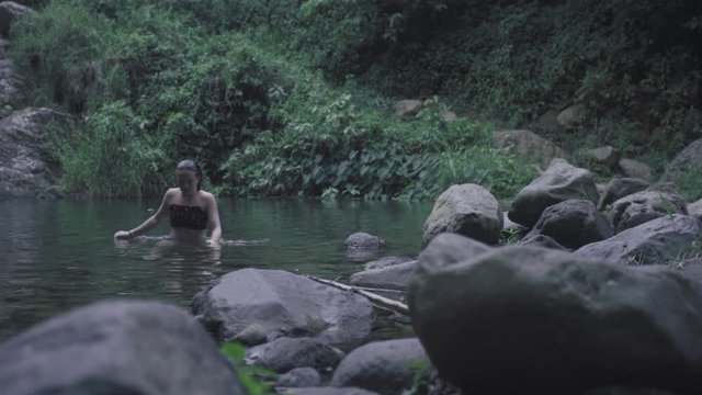 SLOW MOTION: pulling back of rocky terrain as a girl attempts to exit the base of Mango Waterfall in Adjuntas, Puerto Rico.