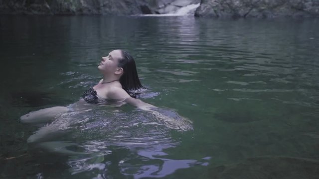 SLOW MOTION: lowering and tilting up as a girl lifts her head out of the water source at the base of Mango Waterfall in Adjuntas, Puerto Rico.