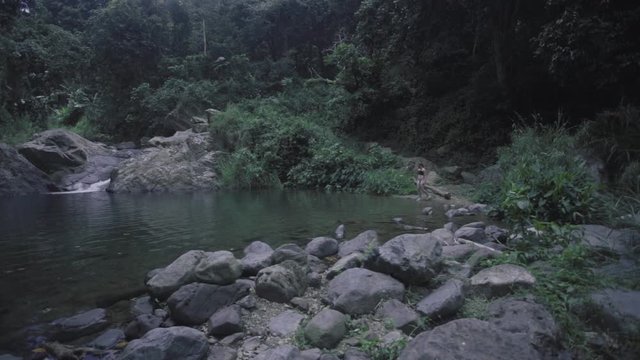 SLOW MOTION: lowering down behind a terrain of rocks as a girl, in the distance, walks into the base of Mango Waterfall in Adjuntas, Puerto Rico.