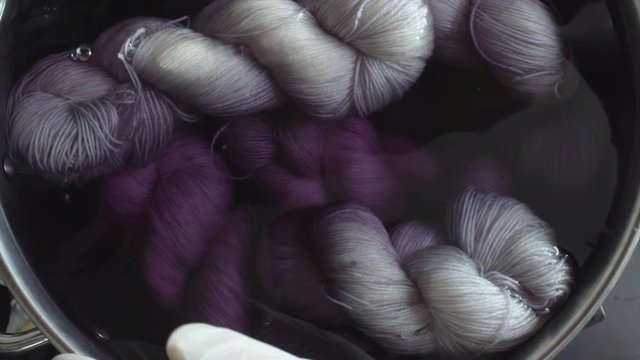Top down slow motion view of someone mixing skeins of yarn in a pot filled with dye and water