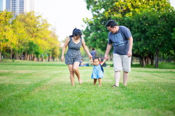 Happy family in the park, Parents holding baby hands walking on the grass field 
