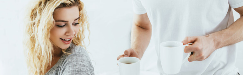 panoramic shot of man holding cups with coffee near attractive blonde woman