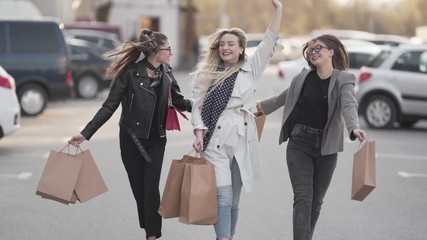 Beautiful female friends walking in the street, waving their shopping bags like shopoholics. Women are energetic, smiling and lauging. Girlish concept - Powered by Adobe