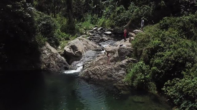 AERIAL: slow lift up and pull away from a girl and boy standing on a rocky structure that's apart of Mango Waterfall in Adjuntas, Puerto Rico.