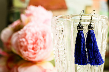 Dark blue earrings tassels close up view with colorful bouquet on blurred background. Female concept of accesseries.